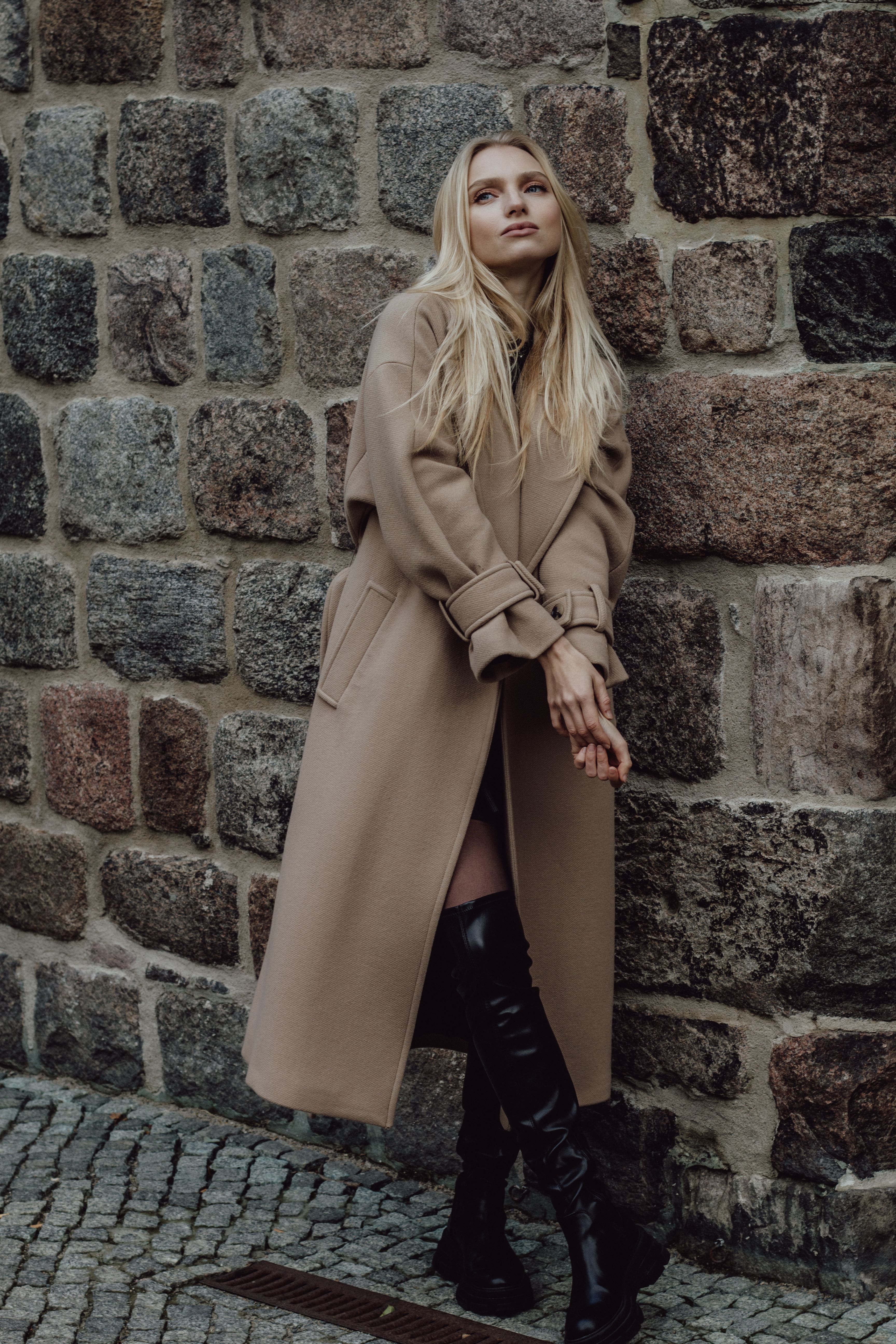 Stylish portrait of a blonde woman in a coat, exuding fall fashion against a stone backdrop.