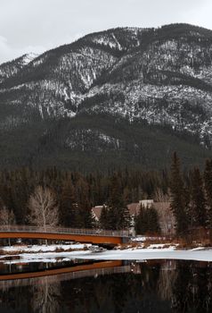 Snow-dusted mountains and a tranquil lake surround a rustic bridge in Banff National Park.