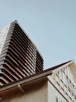 Capture of modern skyscraper juxtaposed with traditional building under clear sky.