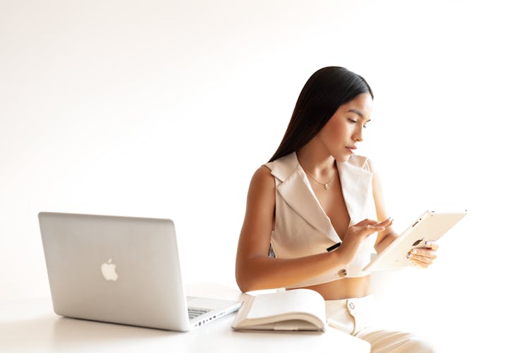 Young Woman Sitting At The Table With A Laptop And Tablet 