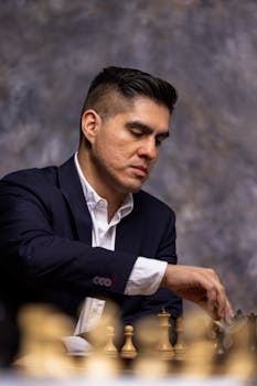 A focused man in a suit playing chess against a gray backdrop.