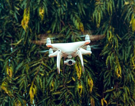 A white drone hovers in the air with a backdrop of lush green foliage in Ekiti Division, Nigeria.