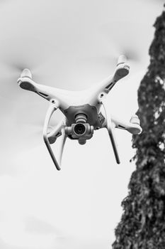 Black and white image of a drone hovering against the sky with blurred propellers.