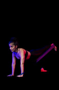 Woman in athletic wear using a resistance band for fitness exercises on a black background.
