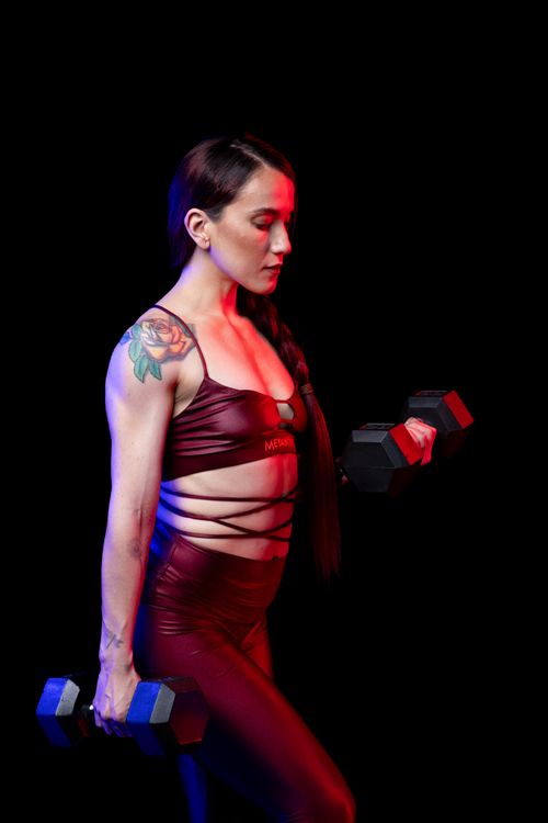 Free Fit woman with tattoos and sportswear lifting dumbbells against a black backdrop. Stock Photo
