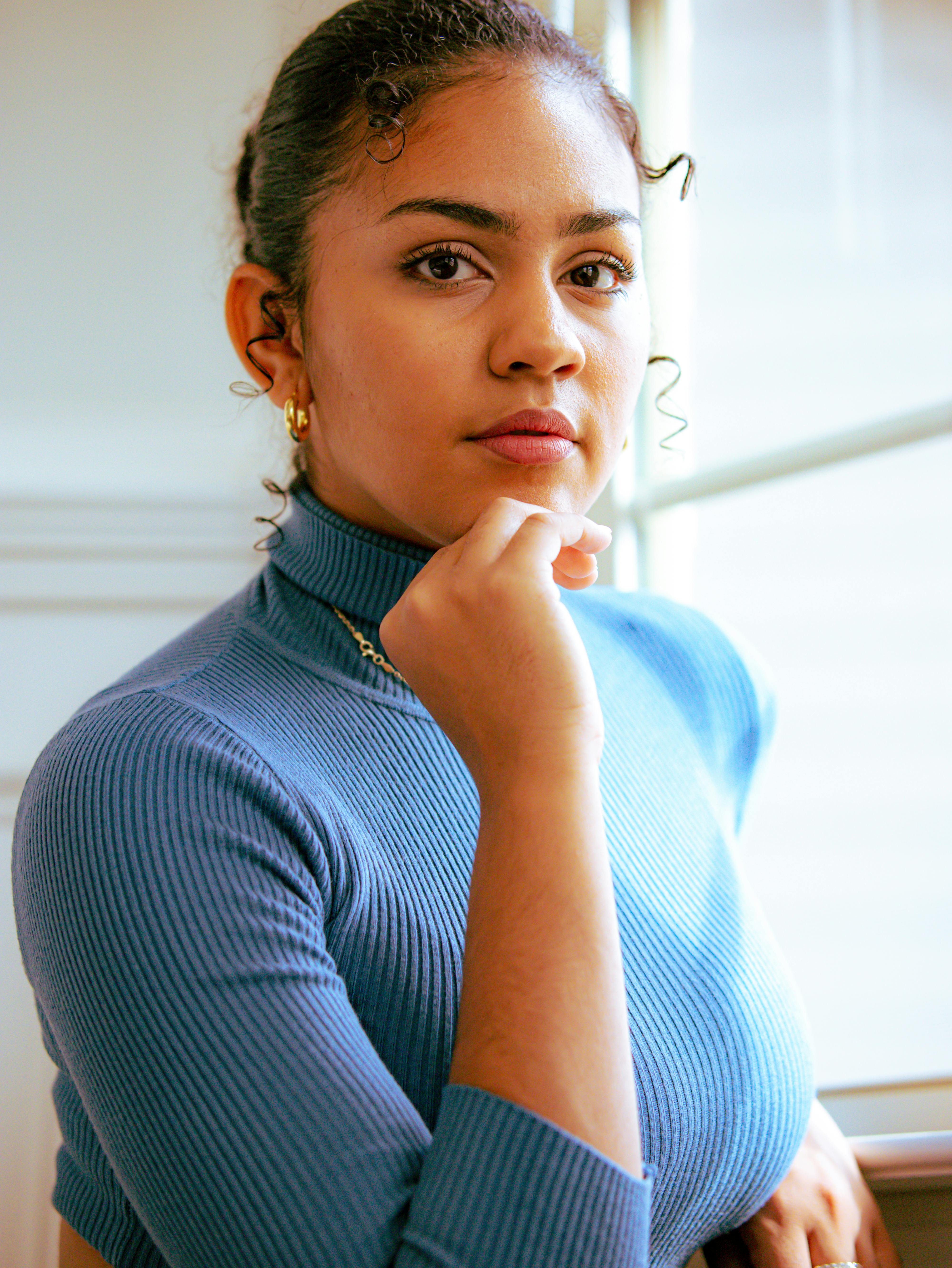 woman wearing blue turtle neck posing by the window