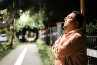 A man in a hoodie stands thoughtfully outdoors at night, illuminated by streetlights.