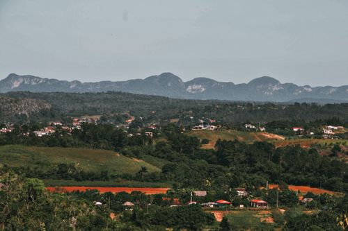 Free Serene countryside landscape featuring lush greenery, rolling hills, and distant mountains under a clear sky. Stock Photo