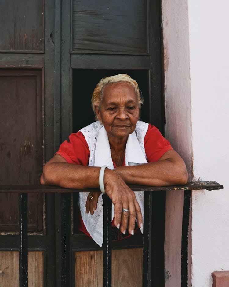 Elderly Woman In The Window Of The Wooden Door Of The French Balcony