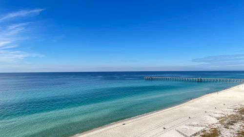 Free Serene beach scene with sandy shore, turquoise ocean, and long pier under clear blue sky. Stock Photo