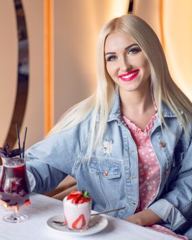 Charming young woman in casual attire enjoying dessert and drink indoors with a bright smile.