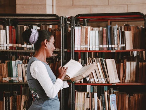 Woman Looking Through a Book at the Library Bookcases