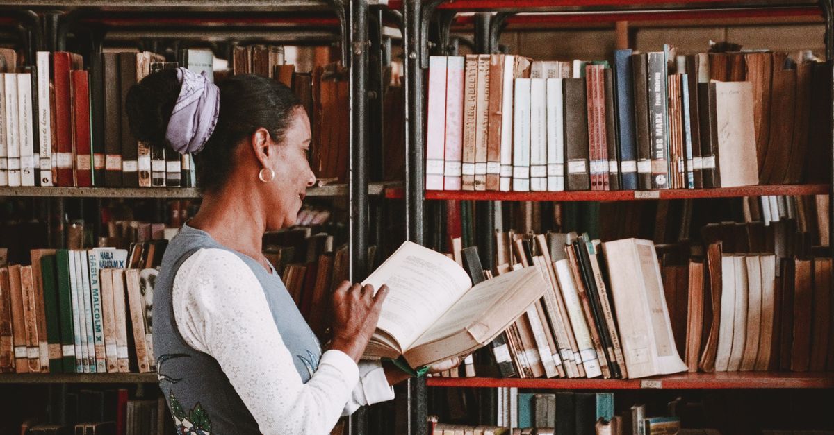 A woman enjoys reading a book in a cozy library filled with bookshelves.