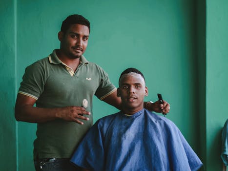 A barber and his client during a haircut session against a green background.