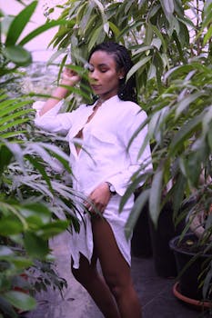 一位时尚女士穿着白衬衫，在户外郁郁葱葱的绿色植物中摆姿势