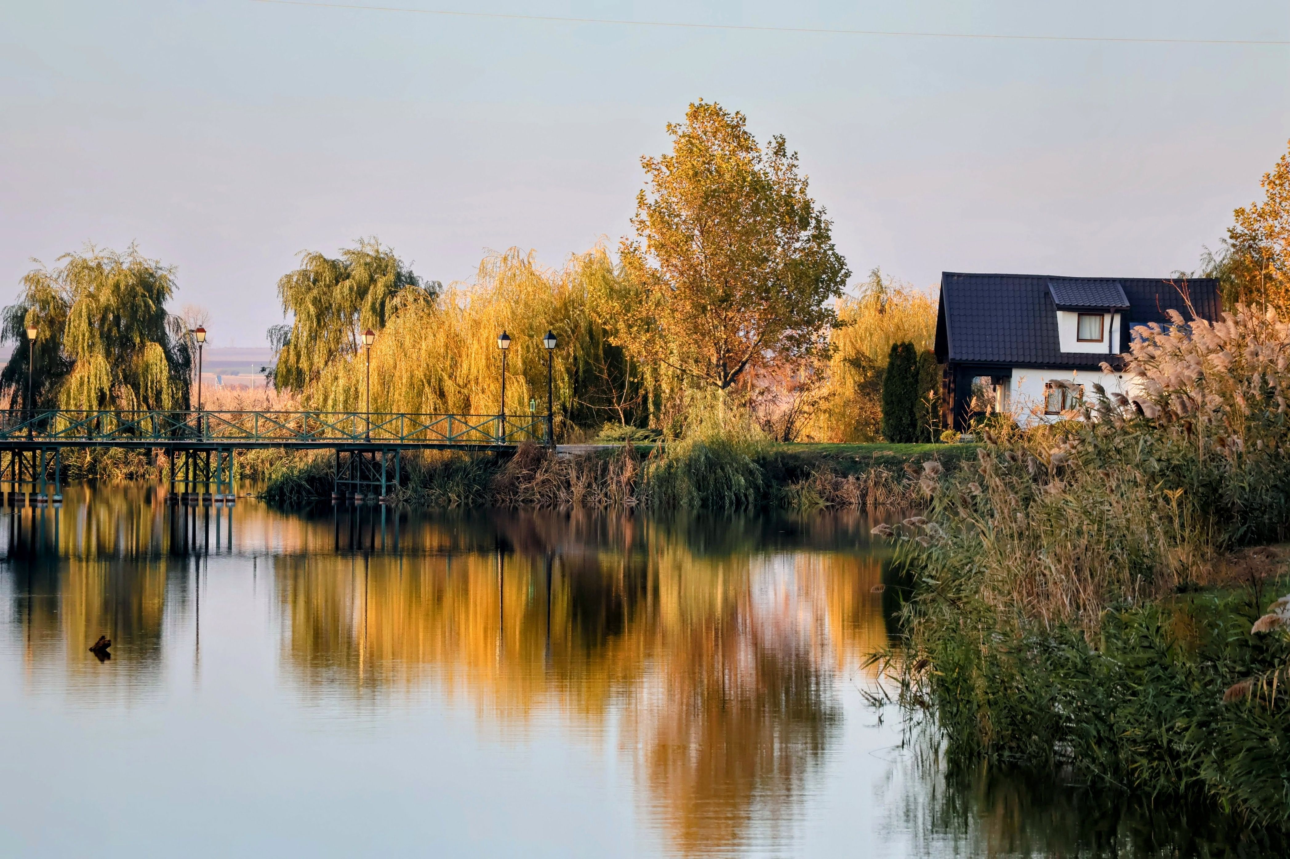 A peaceful rural scene with a lake, footbridge, and rustic cabin surrounded by autumn trees.