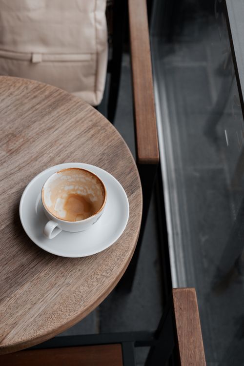 Free An empty coffee cup on a round wooden table by a window in a cozy, modern café setting. Stock Photo
