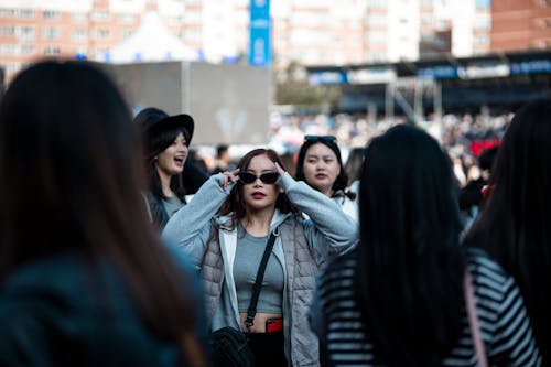 Young Woman with Sunglasses Standing Among Crowd on Street