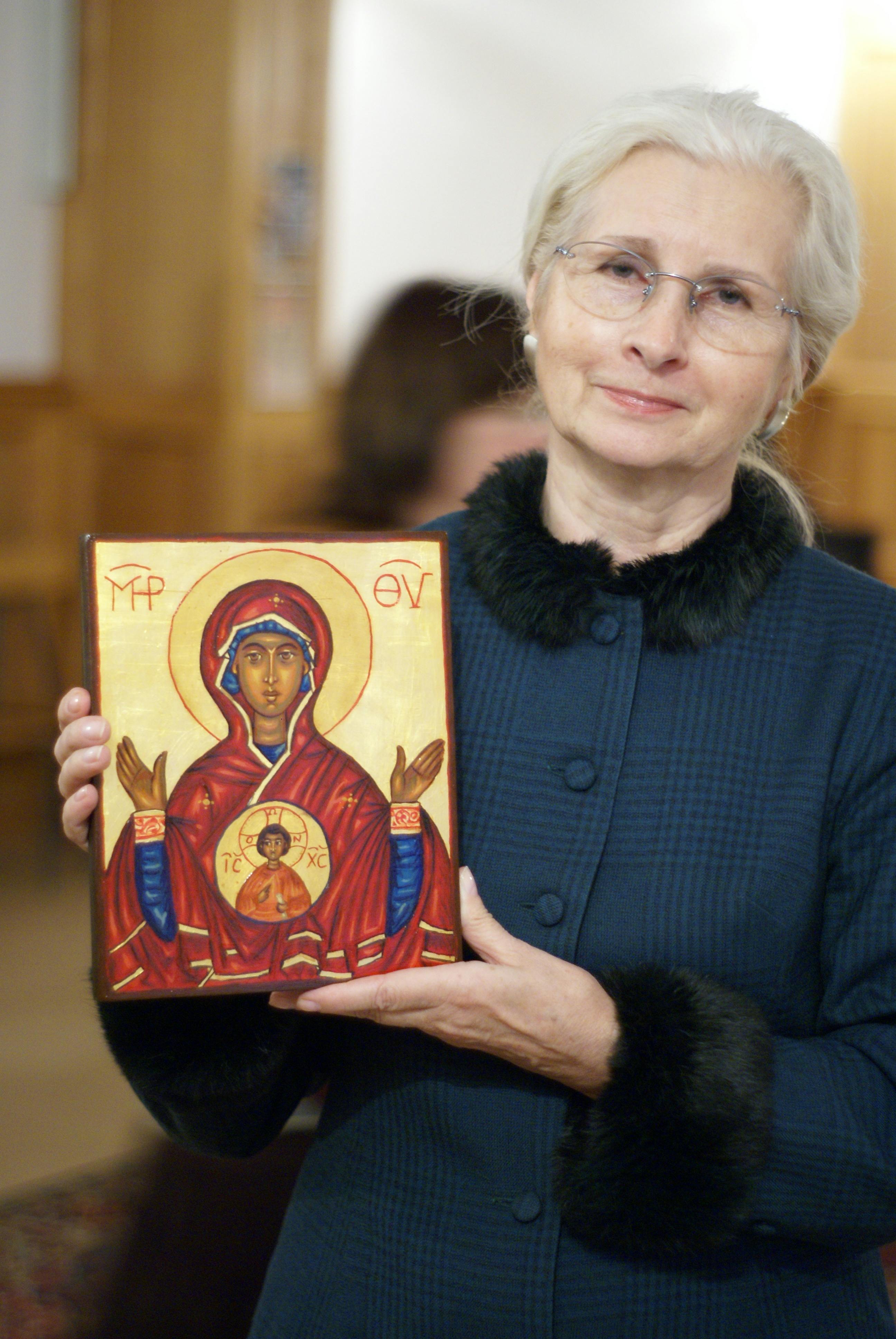 Elderly woman proudly holding an icon of the Virgin Mary, showcasing religious faith.