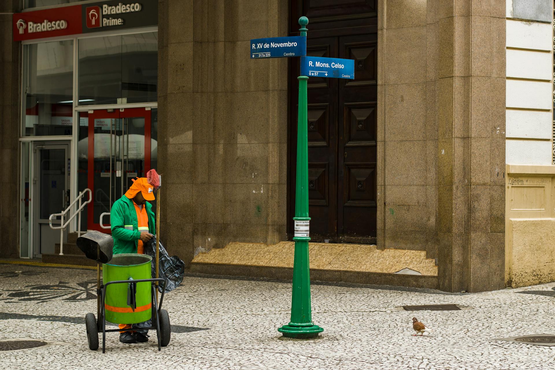 Street cleaner working on a city sidewalk by Bradesco building signs in urban setting.