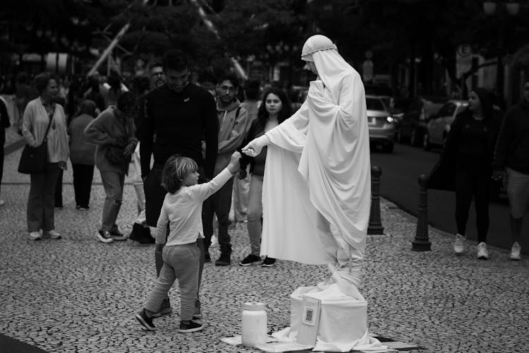 Black And White Photo Of A Person In A White Costume Performing On A Street