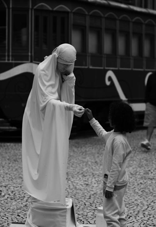 A Child Standing in front of a Person in a Gown on the Street 