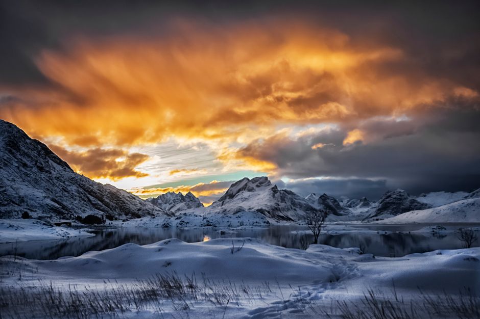 Stunning sunset over snow-covered mountains and lake in Lofoten, Norway.