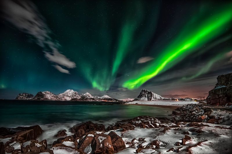 Aurora boreală cu reflexii verzi pe cerul nopții deasupra unui peisaj arctic