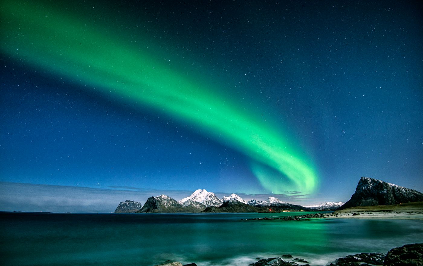 Green and blue aurora borealis over snow-capped mountains in Lofoten, Norway, at night.