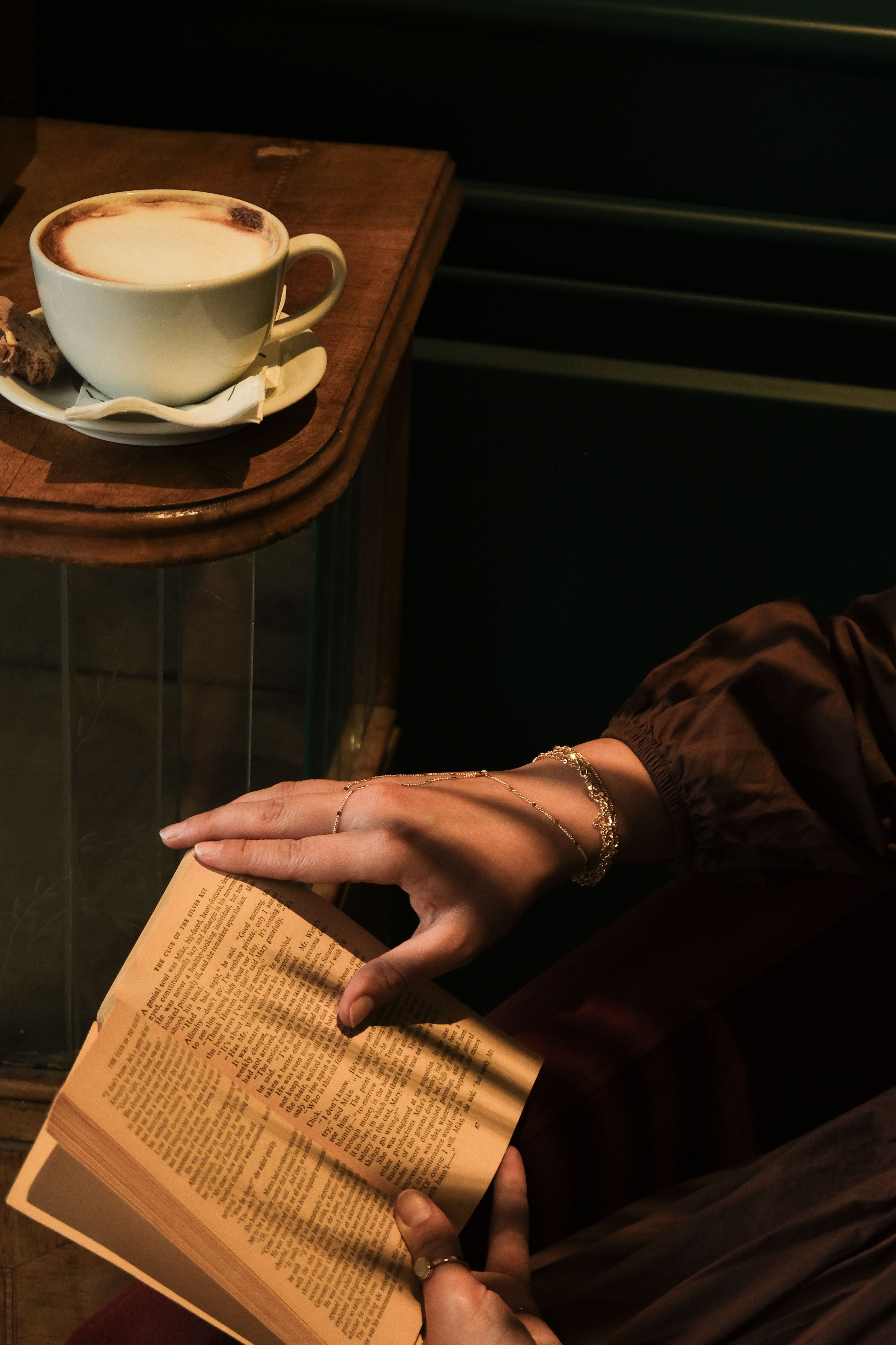 Cozy scene of a person enjoying a cappuccino and reading a book in a cafe.