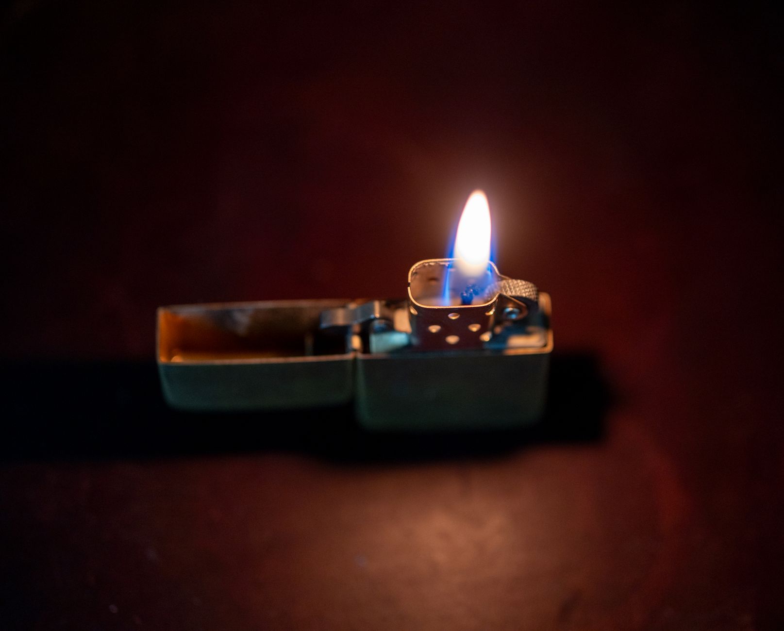 A distinctive metallic lighter with a bright flame against a dark background.