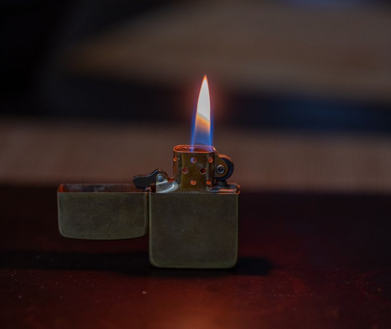 Captivating image of an open metallic lighter with a bright flame against a dark background.