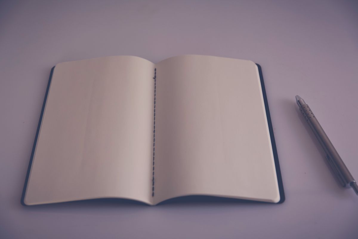 A close-up of a paper notepad on a desk with a pen and a pair of glasses beside it