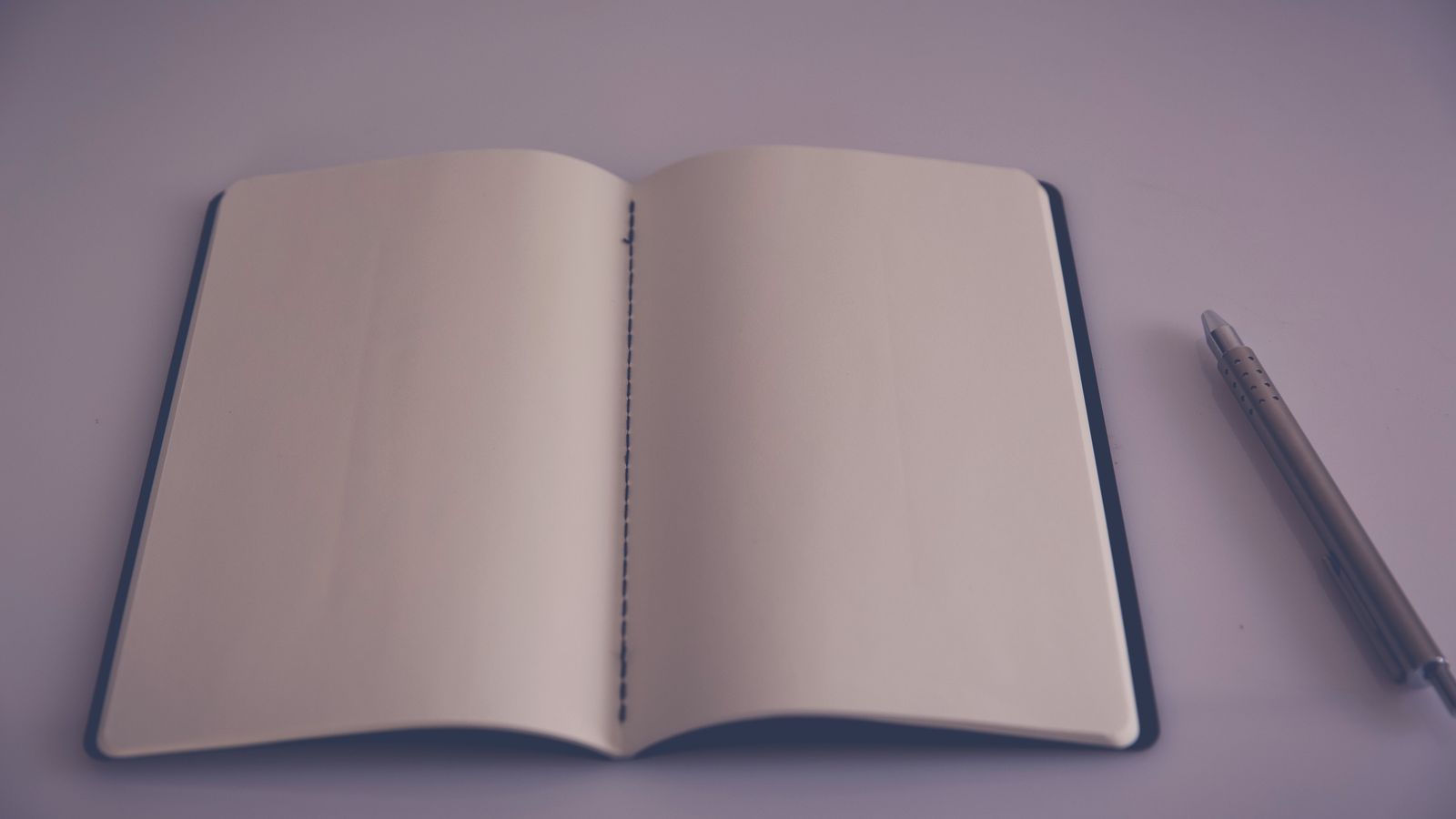 Caderno aberto com páginas em branco e uma caneta.