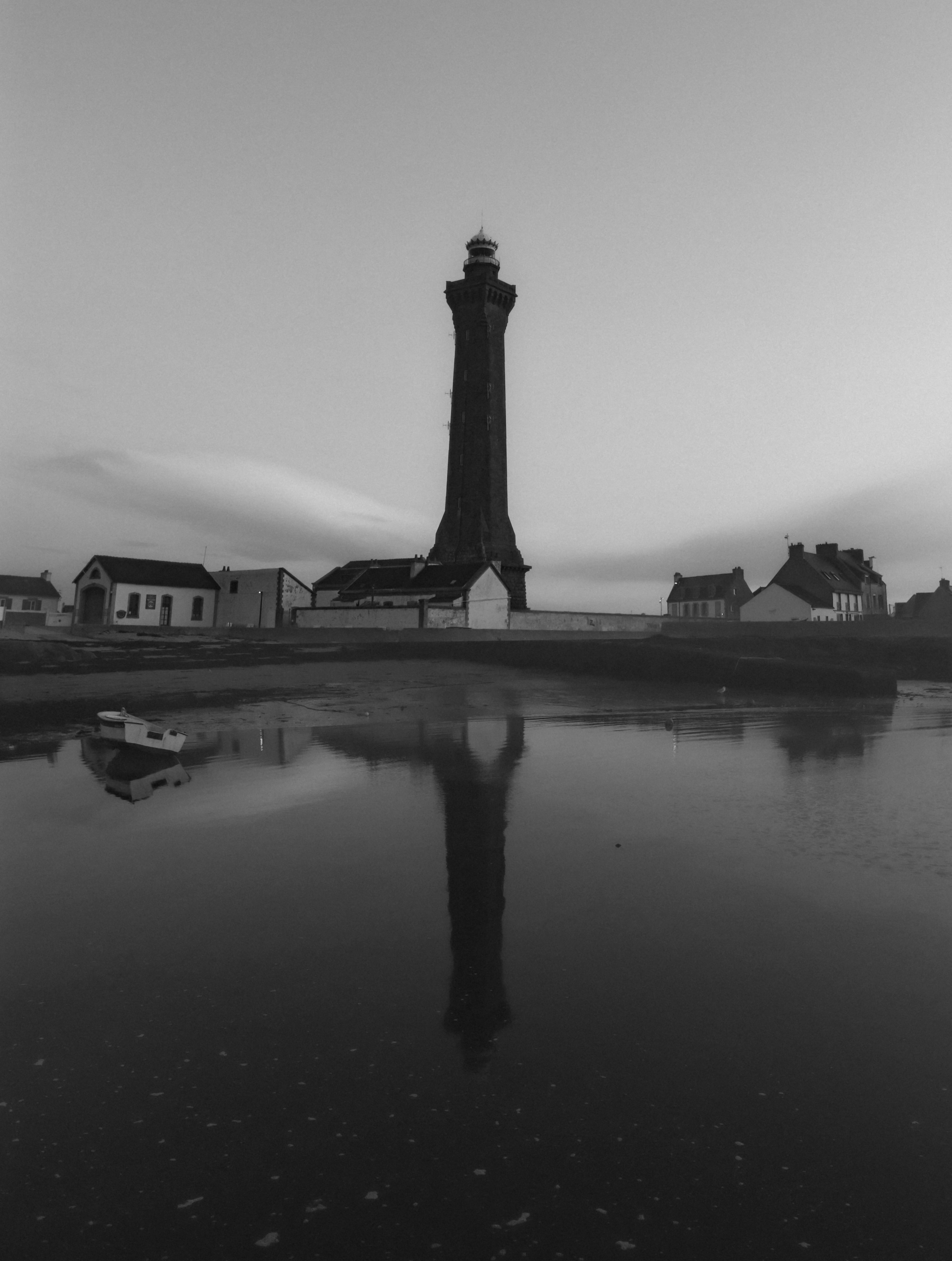 Monochrome capture of Phare d'Eckmühl lighthouse reflecting in calm waters, France.