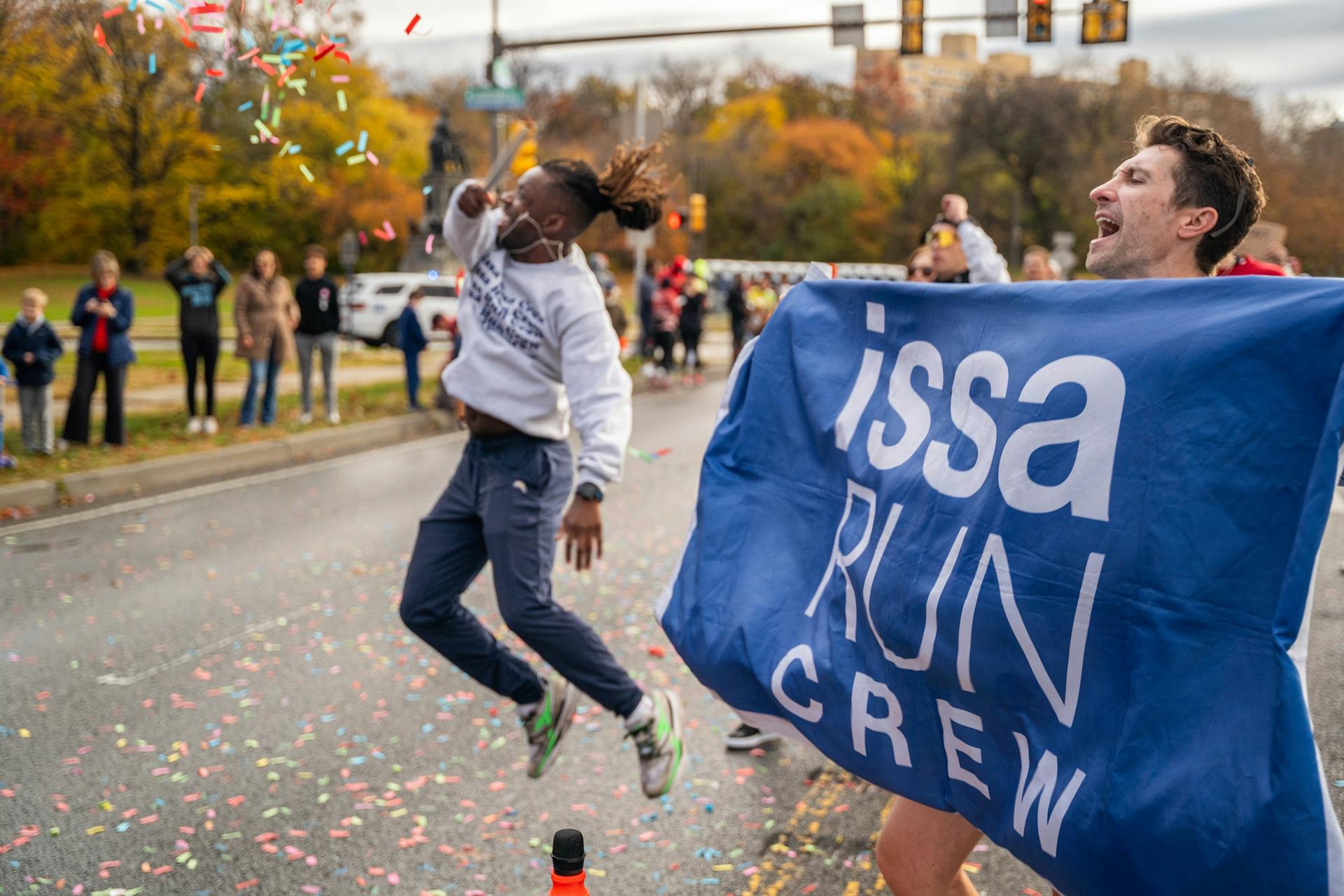 Excited runners celebrate at a vibrant street event with confetti flying in the air, showcasing community spirit.