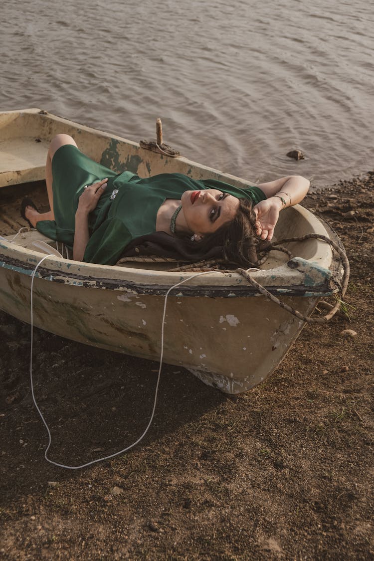 Brunette Woman In Green Dress Posing In Old Canoe On Beach