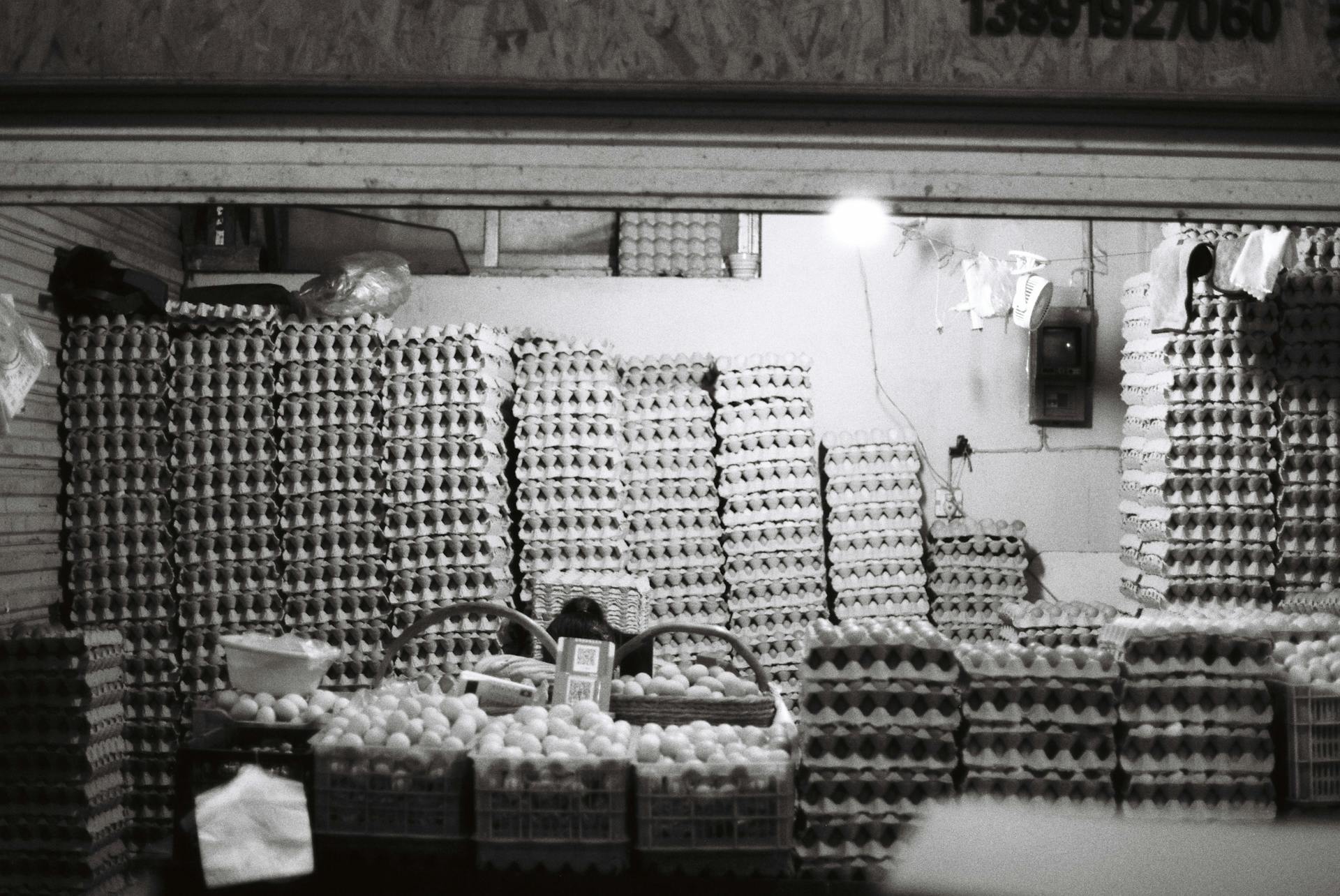 Stacks of eggs in trays inside a market store, captured in black and white.