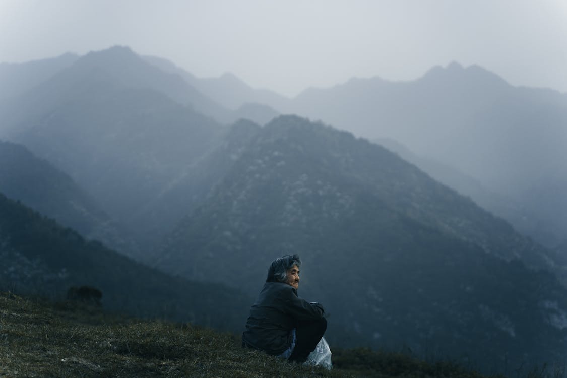 Elderly Woman Sitting on Meadow and Looking at Mountains · Free Stock Photo