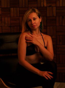 Elegant woman in lingerie poses confidently in a stylish chair against a dark backdrop.