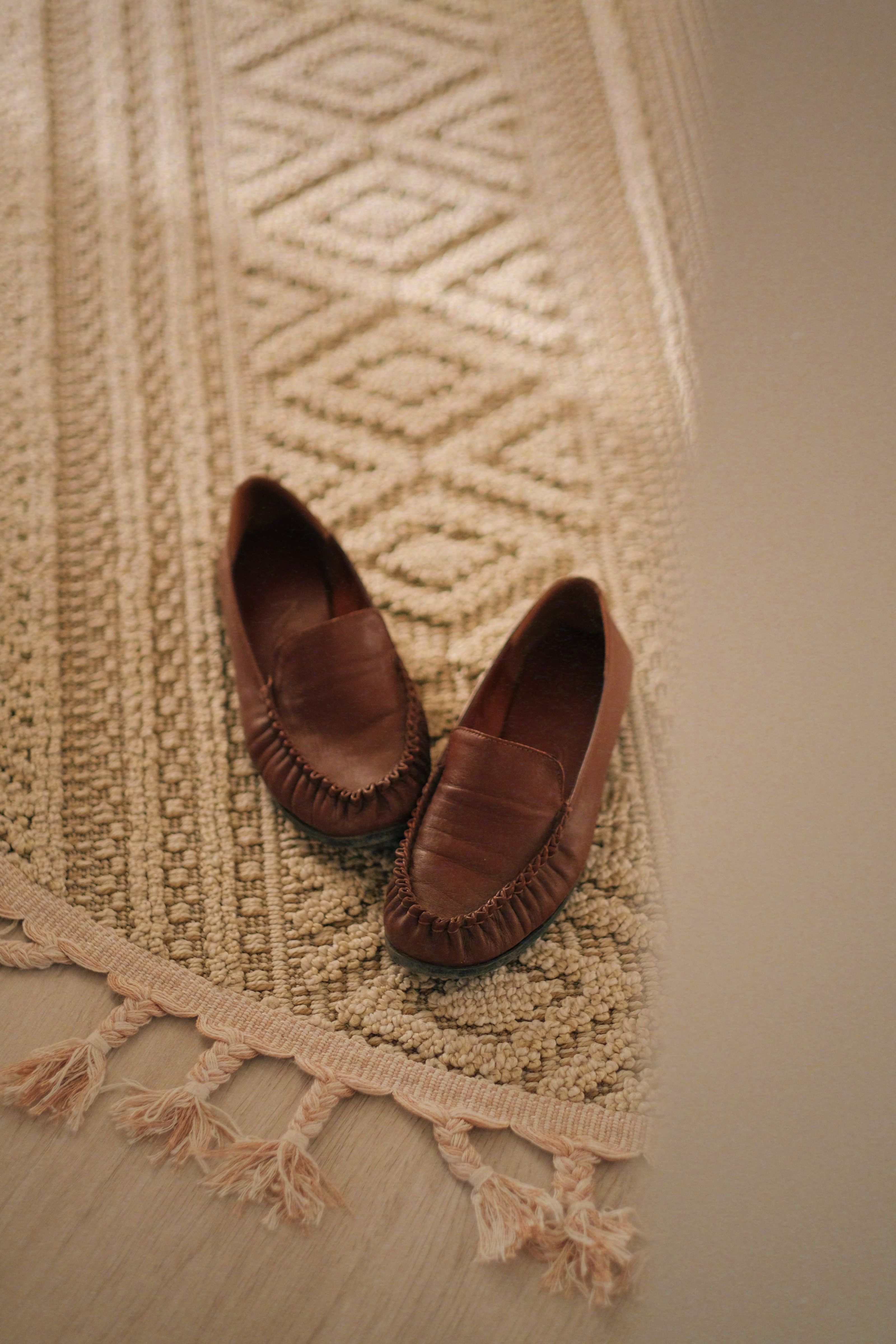 Elegantes mocassins marrons colocados sobre um tapete feito à mão com textura, dentro de casa.