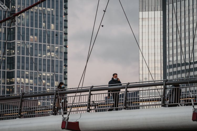 Passersby On A Suspension Footbridge Over A Main River In Frankfurt