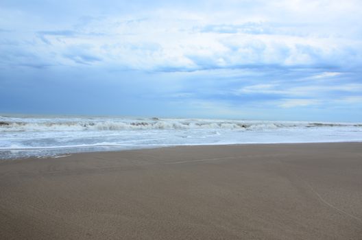 Tranquil sandy beach in Pinamar, Argentina with gentle waves under a cloudy sky.