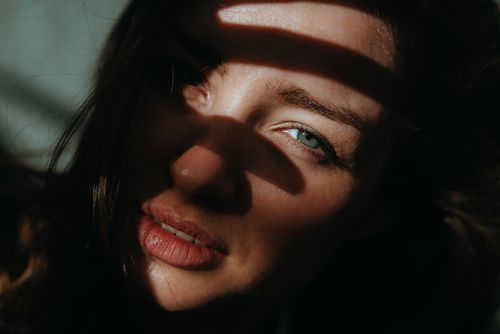 Free A captivating close-up portrait of a woman partially shadowed, highlighting her green eyes and natural beauty. Stock Photo