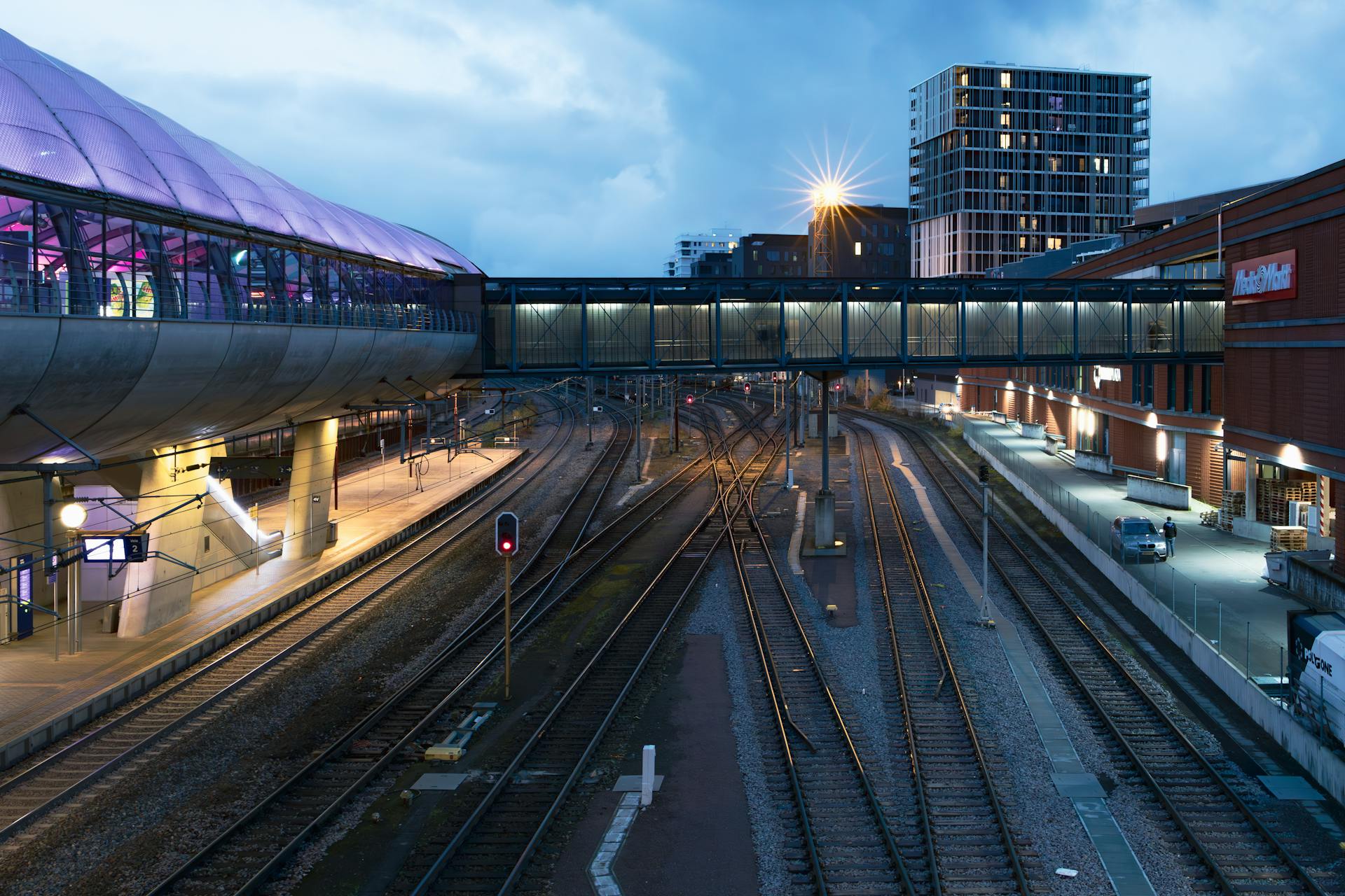 A modern railway station and pedestrian bridge at twilight in Luxembourg cityscape.