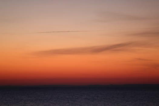 A breathtaking sunset view over a calm ocean horizon, showcasing vibrant orange hues and wispy clouds.