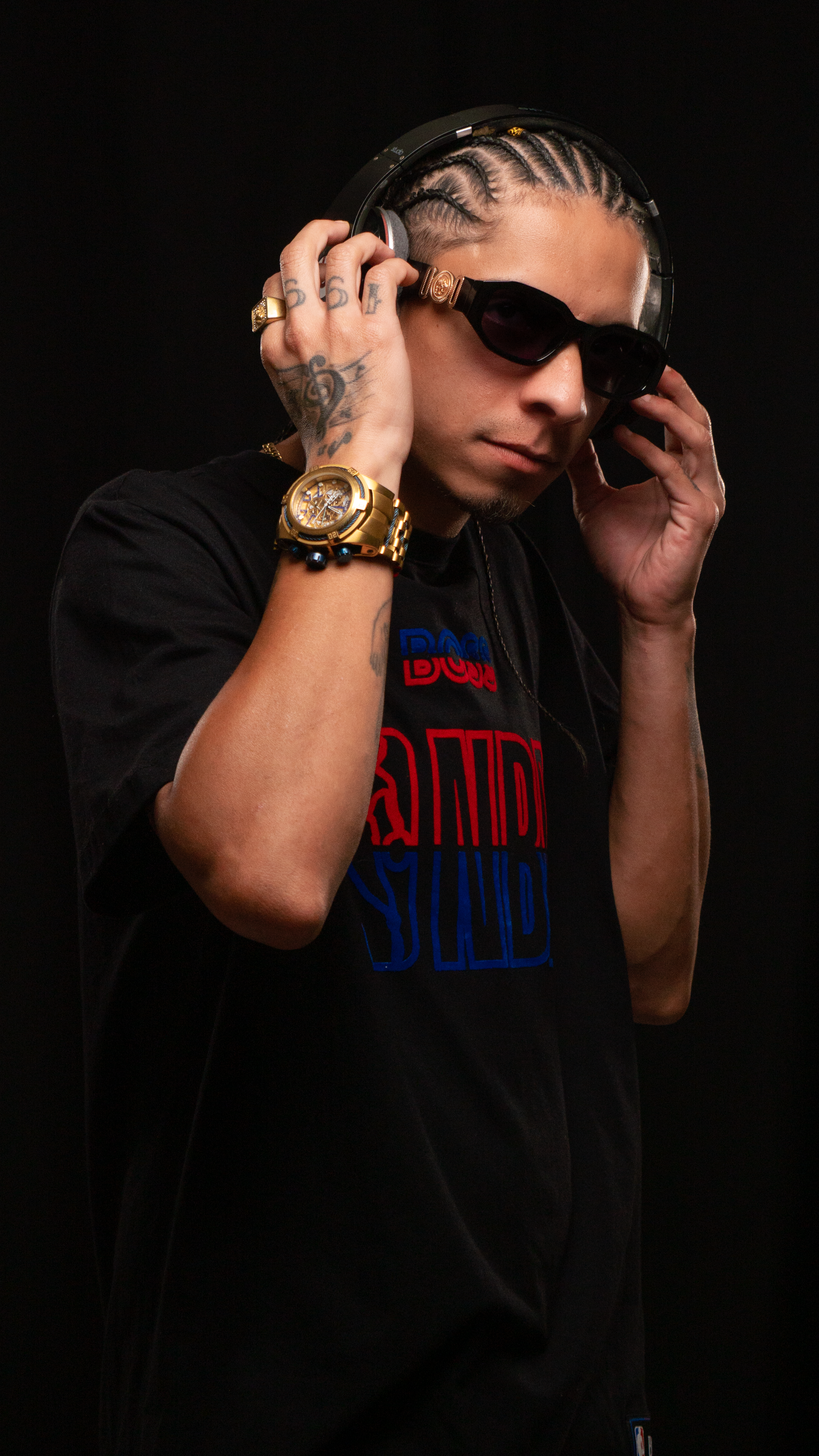 Stylish man wearing sunglasses and headphones on a black background, showcasing street fashion.