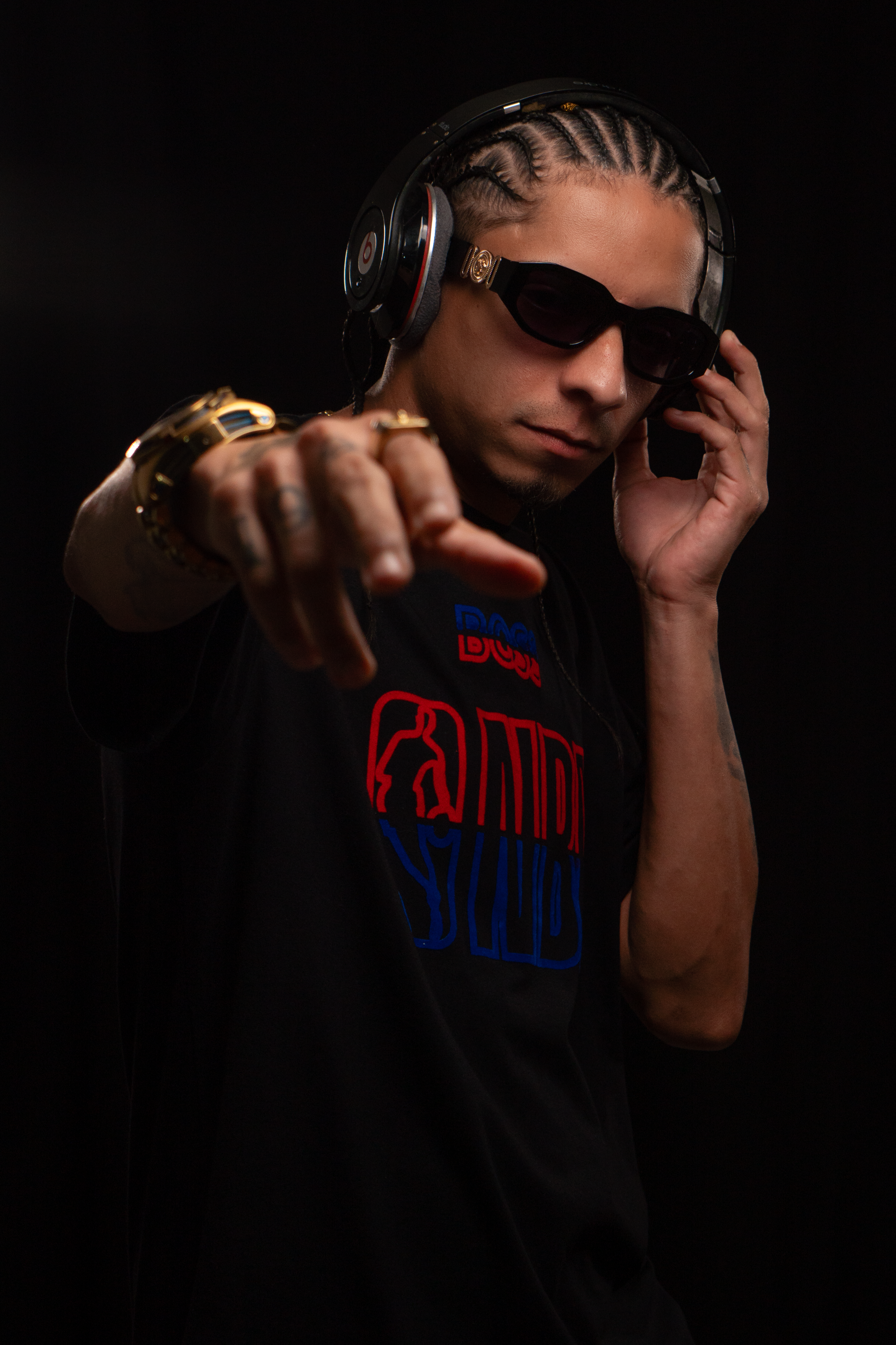 Fashionable young man with headphones and sunglasses pointing, captured in a studio setting on a black background.