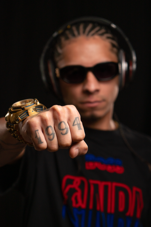 Free Fashionable man with tattoos and accessories posing confidently in a studio setting with a black background. Stock Photo