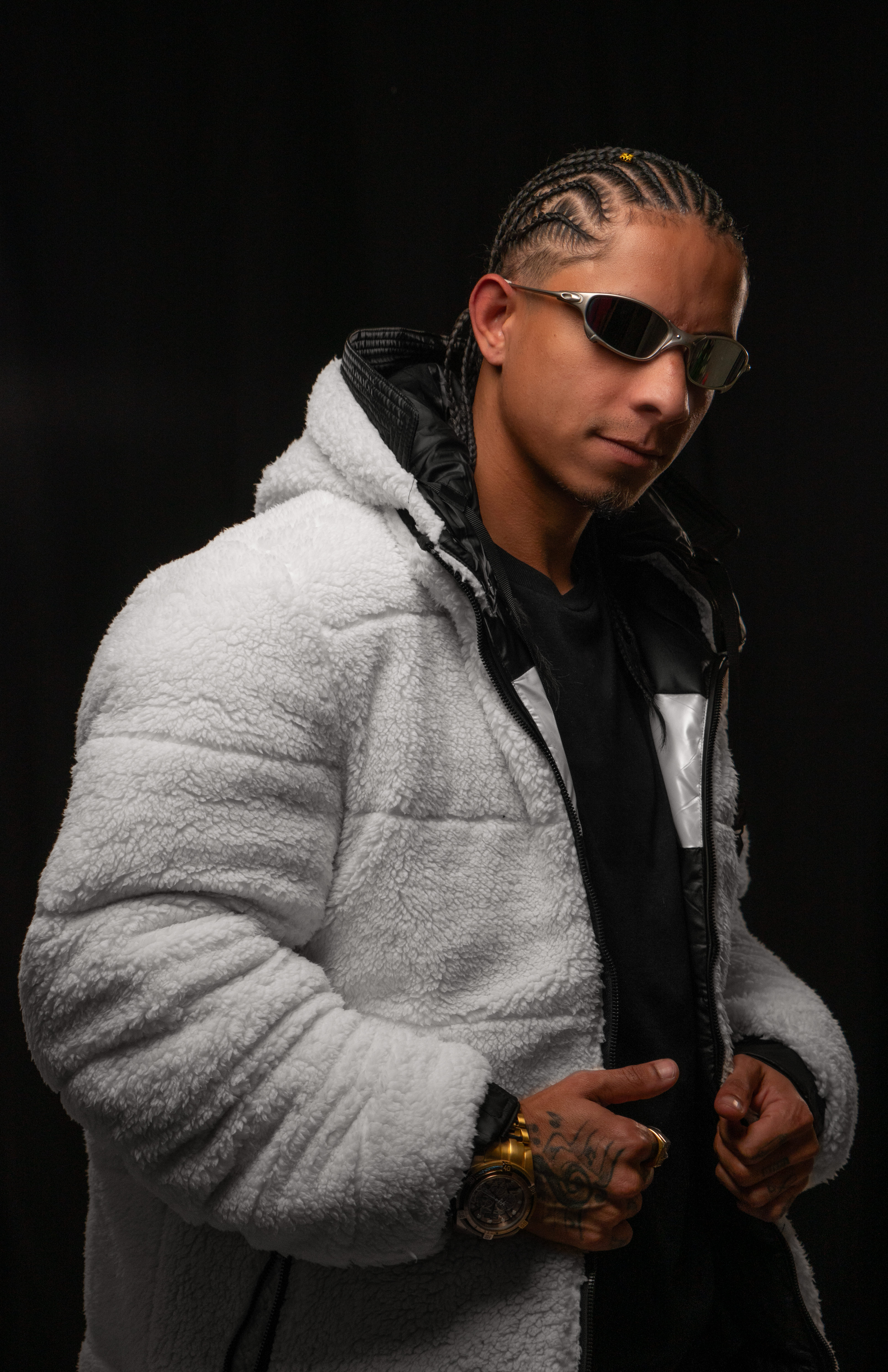 Man in a white jacket and sunglasses striking a confident pose against a dark background.